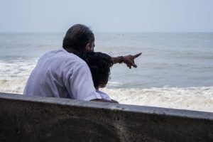 un uomo indica qualcosa in mezzo al mare a una bambina che sta abbracciando su una panchina