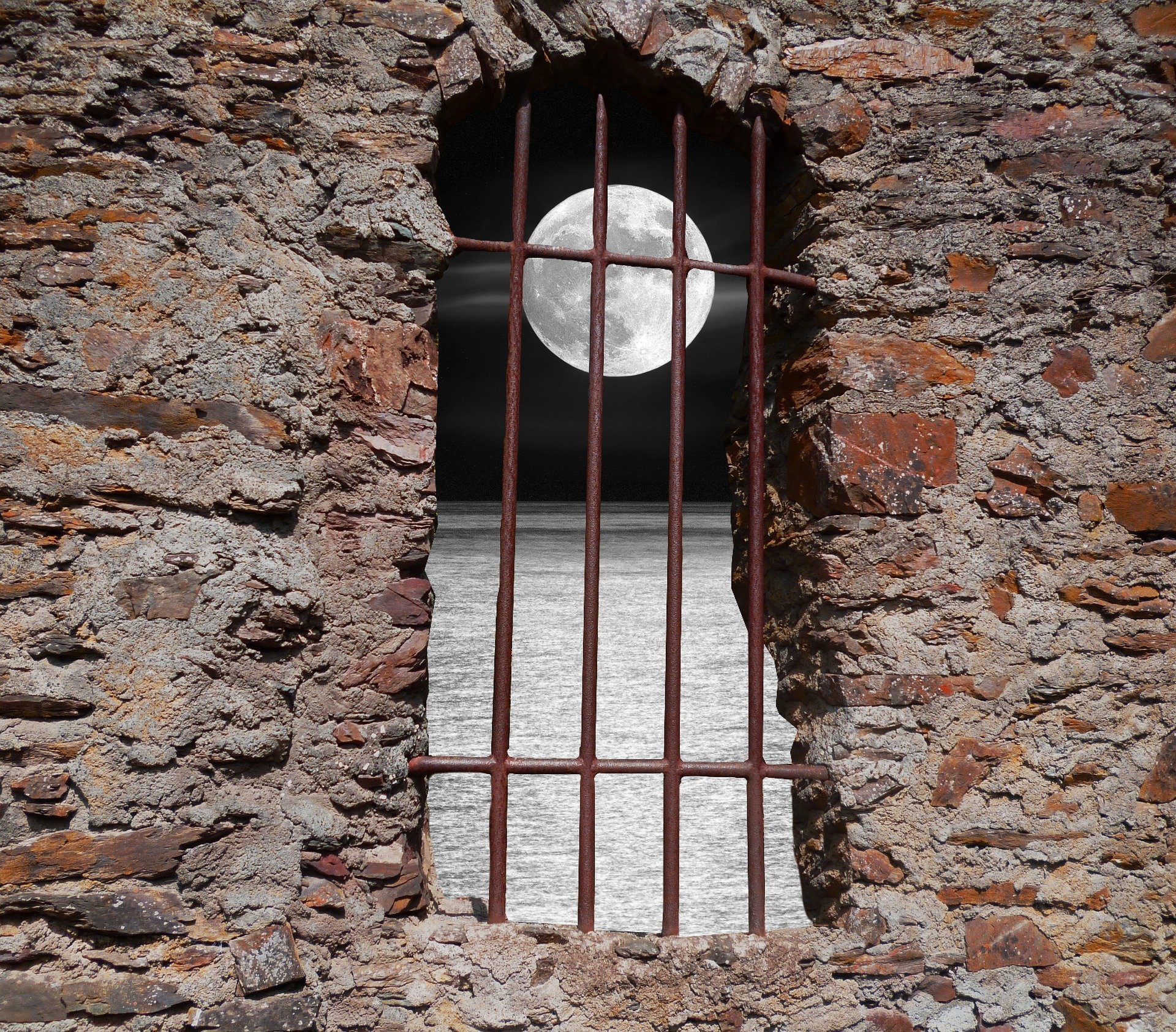 muro in pietra con un'apertura sbarrata a ferro dalla quale si intravede la luna sul mare
