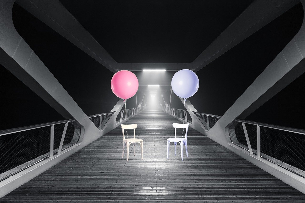 sopra un ponte due sedie con due palloncini uno blu uno rosa in immagine in bianco e nero