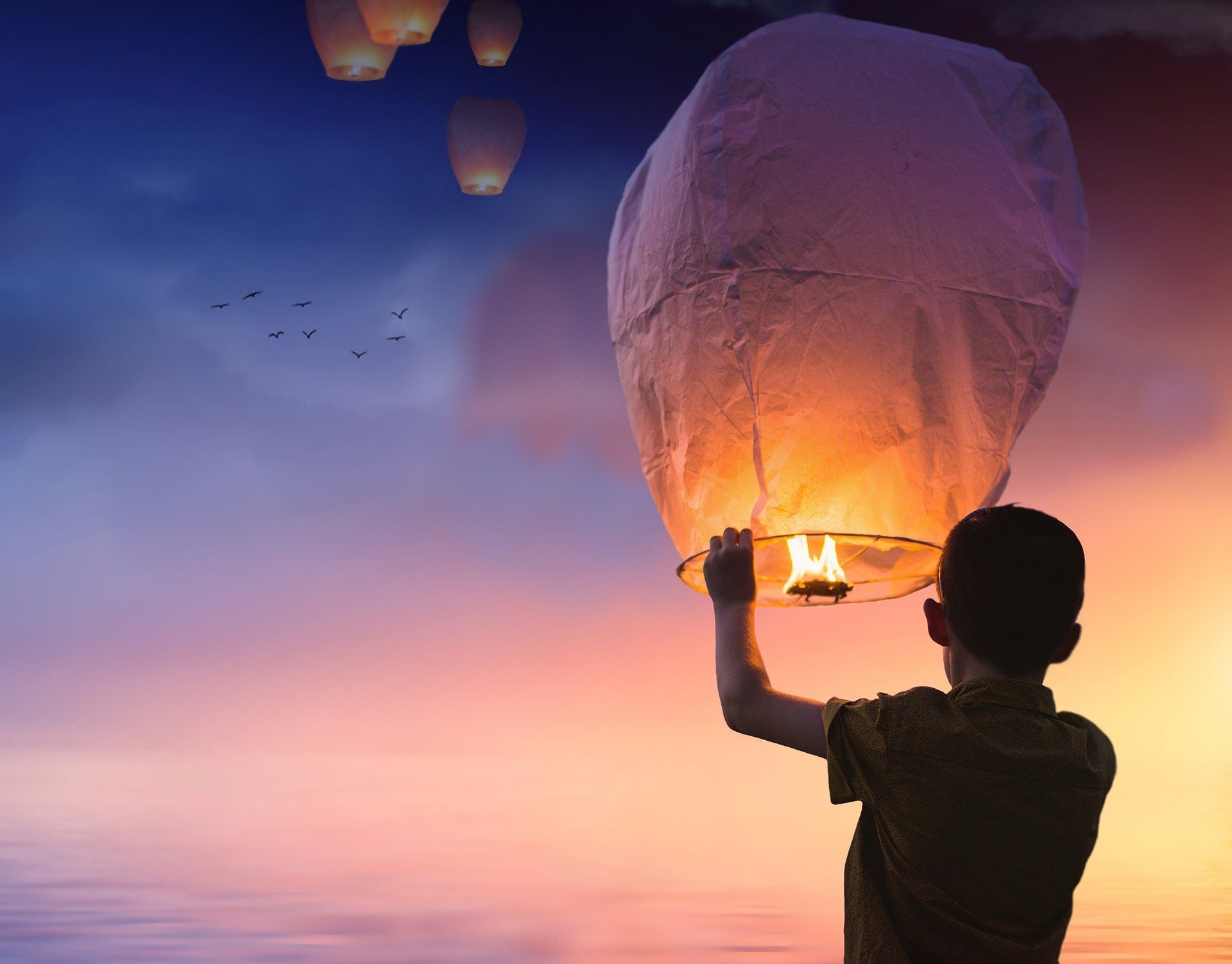 un bambino di spalle che al tramonto fa volare una lanterna in cielo