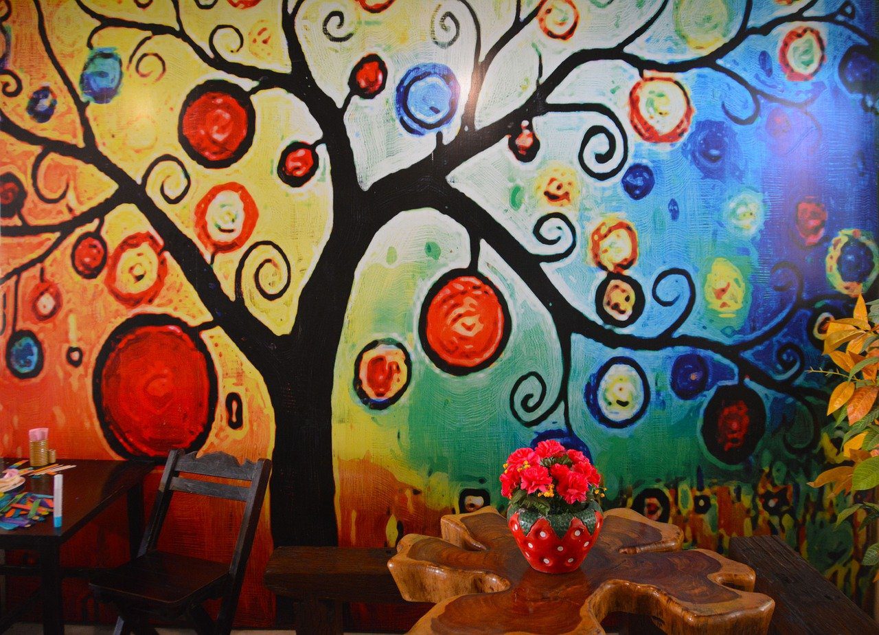 un ambiente scolastico per bambini con albero disegnato alla parete,tavolo fatto a tronco d'albero,vaso di fiori a forma di fragola e matite colorate su un altro tavolino