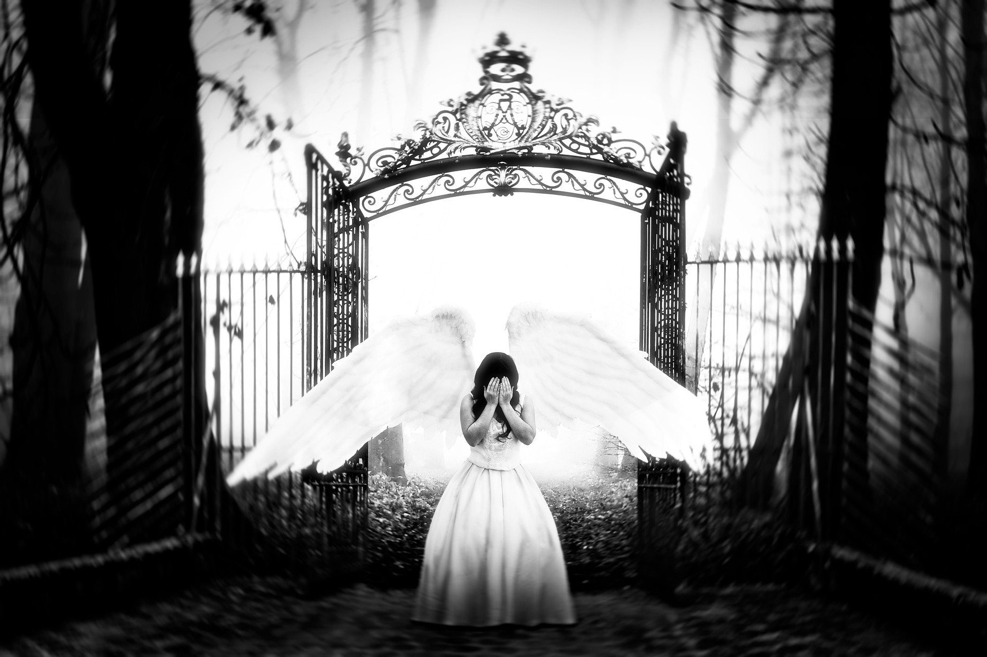una donna angelo che si copre il viso come per piangere scacciata dal paradiso cn alle spalle un enorme cancello, immagine in bianco e nero