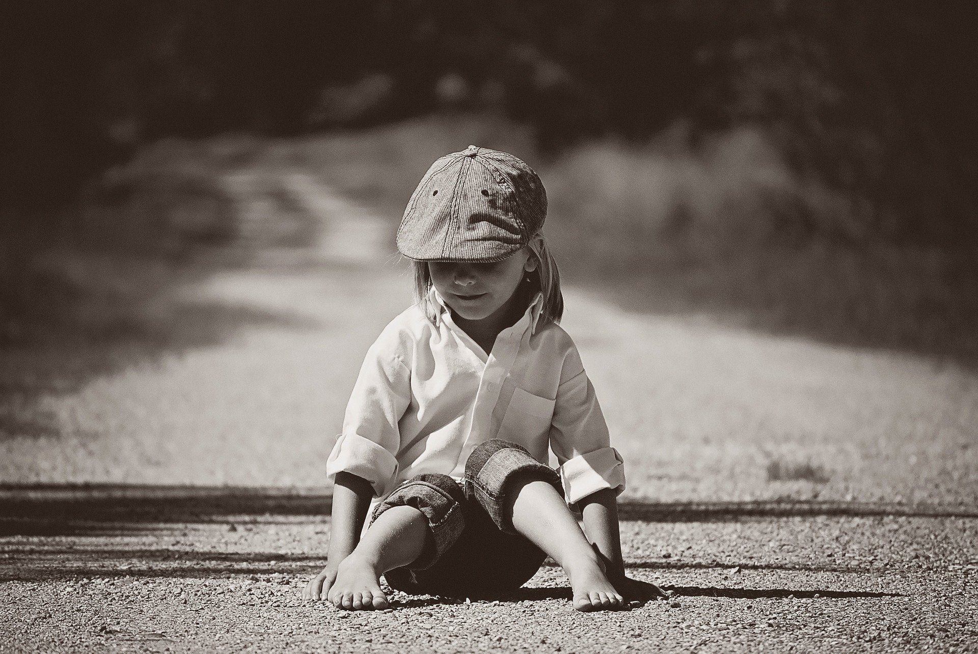foto in bianco e nero un bambino con cappello seduto in mezzo alla strada