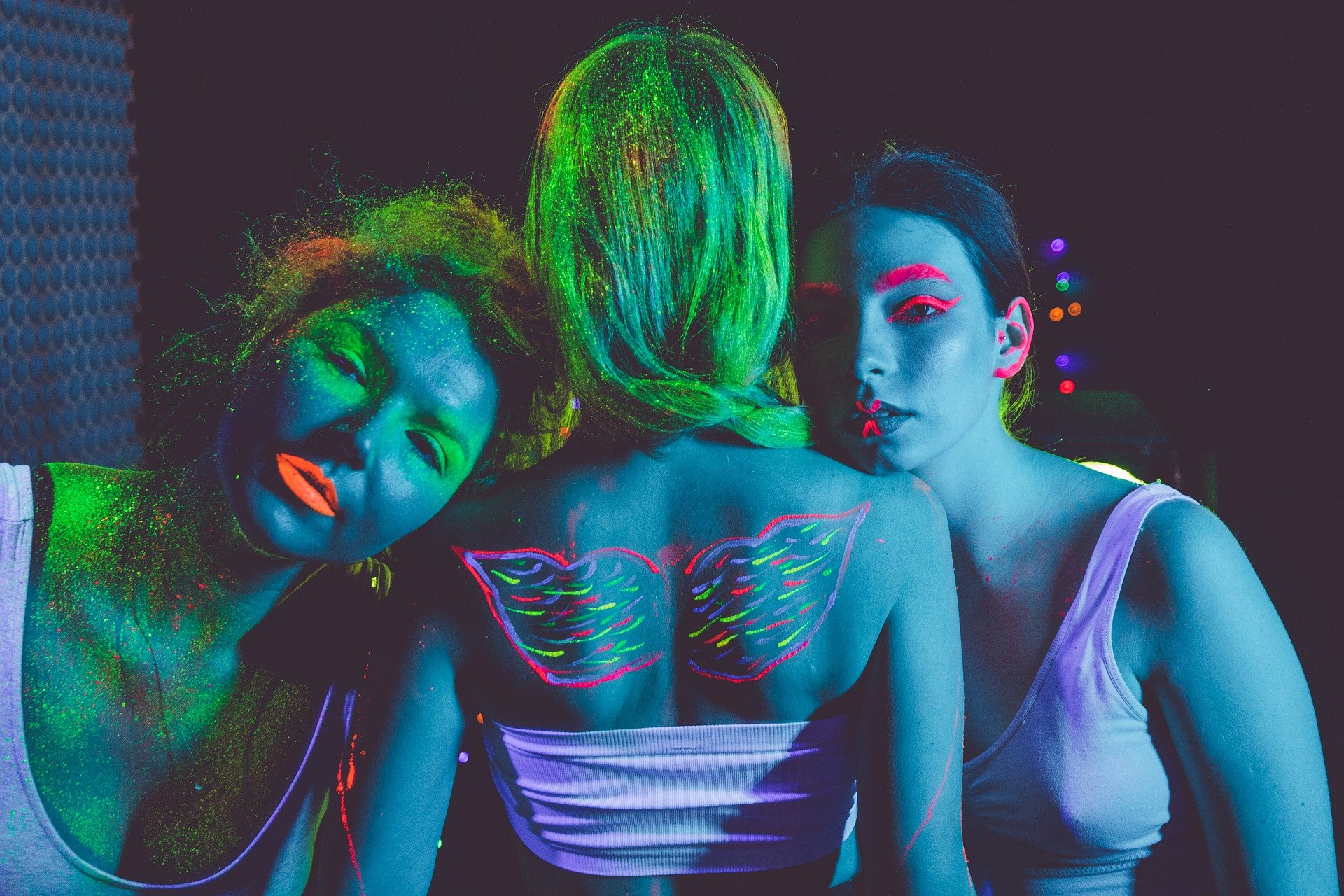 tre ragazze col corpo dipinto di blu e da disegni fluo addosso, di cui una di spalle