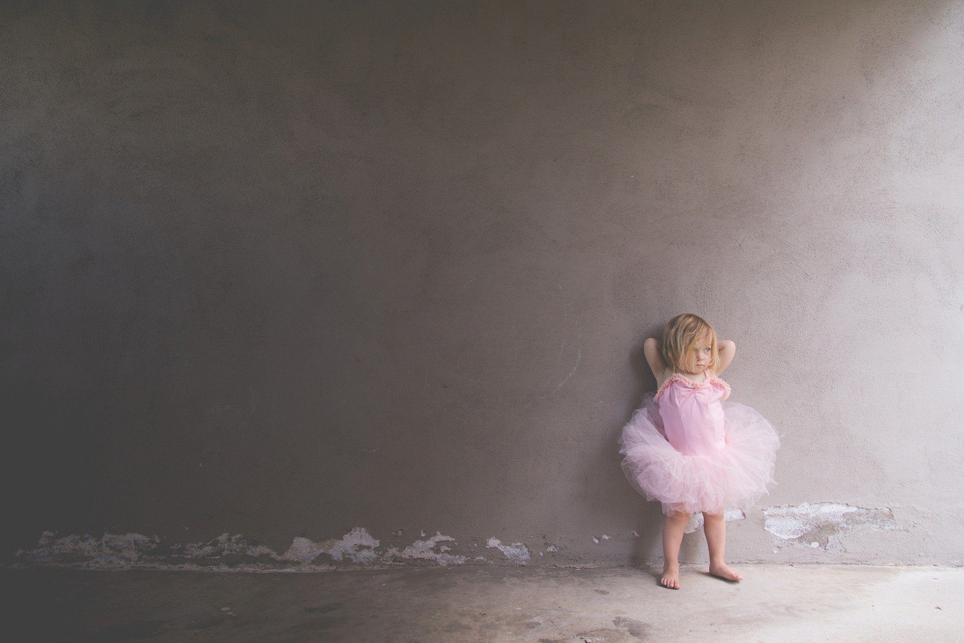 una bambina in tutù appoggiata ad un muro grigio e rovinato