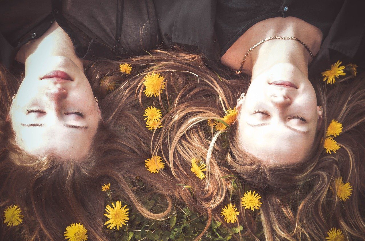 volto di due ragazze sdraiate a terra vicine con margherite sparse tra i capelli