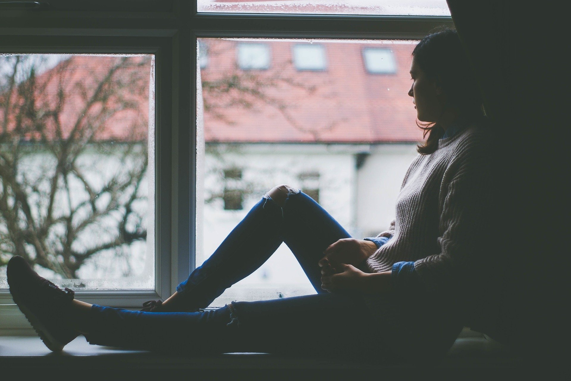 una donna seduta sul davanzale di una finestra mentre guarda fuori
