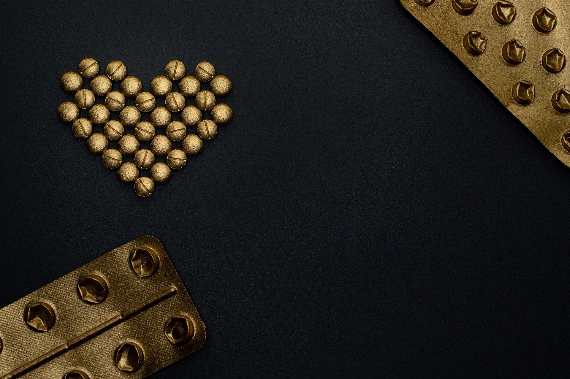 su sfondo nero, blister di pillole color oro e pillole color oro disposte in modo da formare un cuore