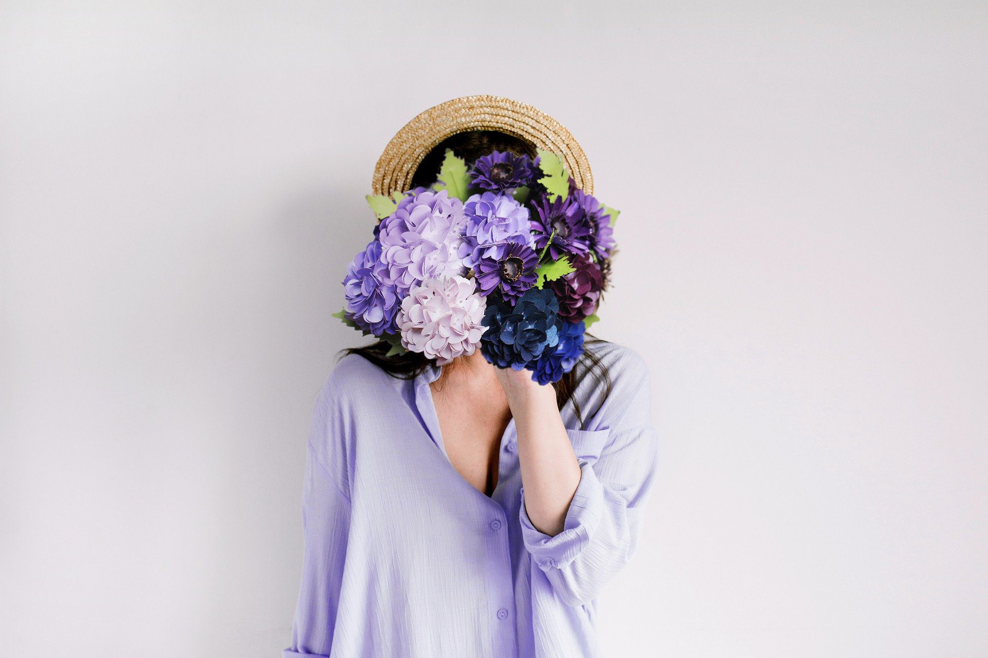 donna con cappello e maglia lilla, con un mazzo di fiori tonalità viola davanti il volto